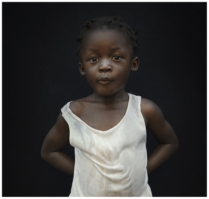 Portrait von einem schwarzen Kind mit weissem Unterhemd vor schwarzem Hintergrund