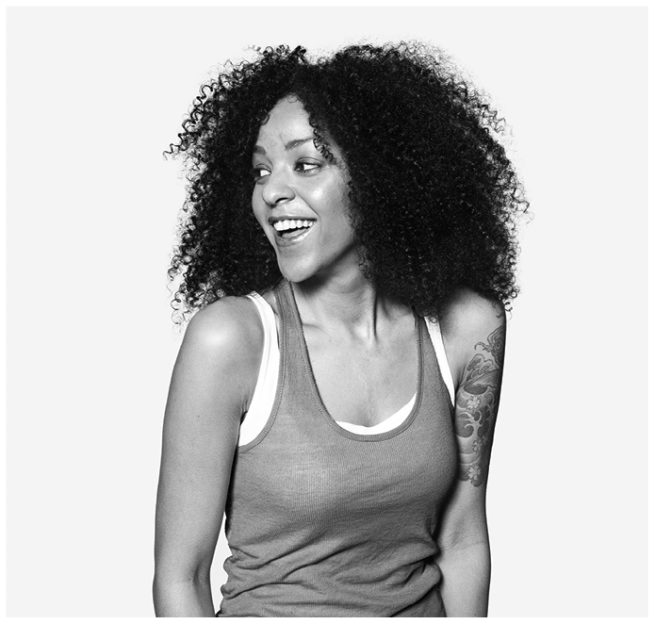 Schwarz weiss Portrait einer lachenden jungen farbigen Frau mit Tattos vor weissem Hintergrund