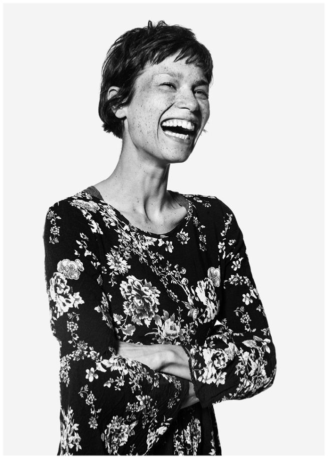 Portrait von Amber Pine im Blumenkleid lachend im Studio vor weissem Hintergrund