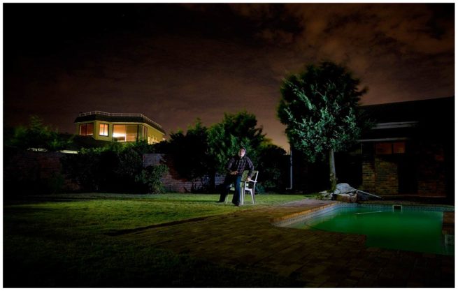 Nachtaufnahme eines Mannes der erschrocken von seinem Stuhl aufsteht und nach oben schaut