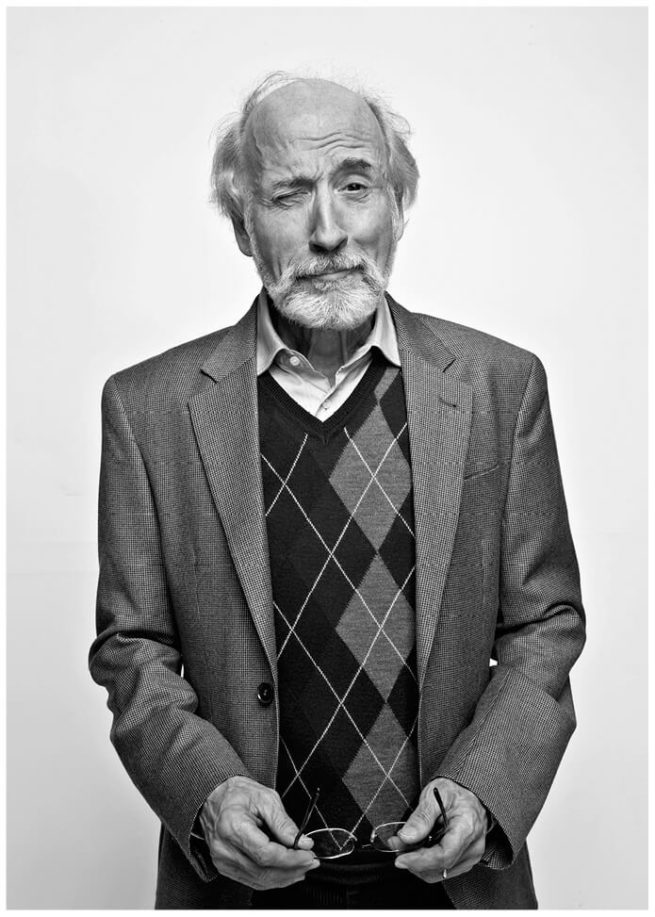 Schwarz weiss Portrait von einem älteren Mann vor weissem Hintergrund im Studio. Der Mann schaut skeptisch in die Kamera