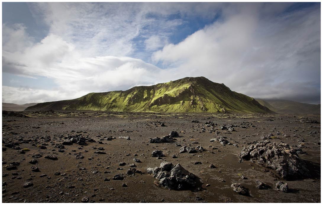 Grüner Berg in karger Vulkanlandschaft auf Island