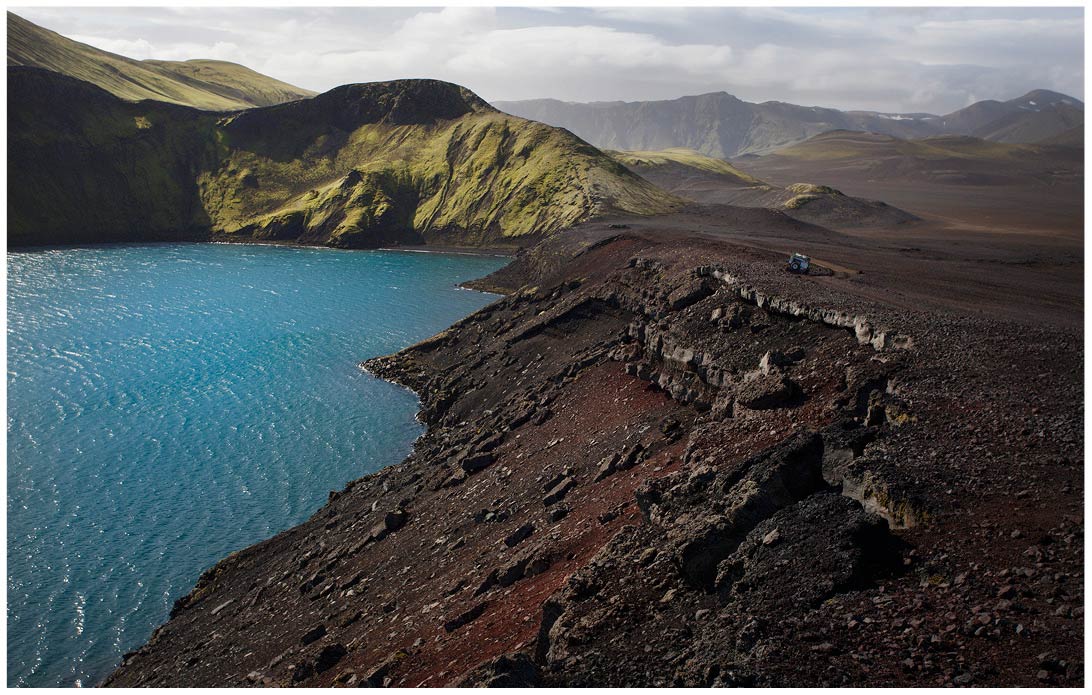 Türkiser See in Island neben rotem Geröll und grünen Felsen