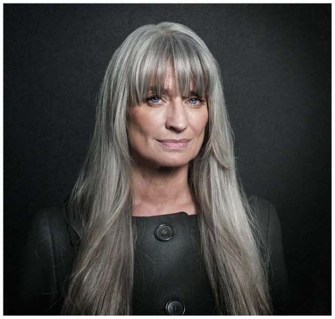 Studioportrait einer Frau mit langen grauen Haaren vor schwarzem Hintergrund
