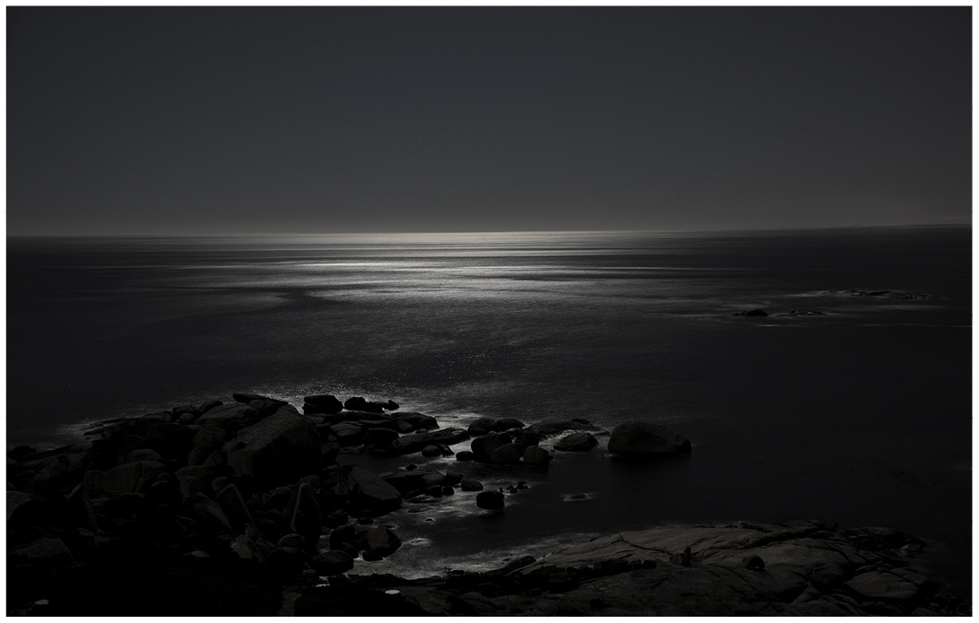 Nachtaufnahme von einem felsigen Strand bei Mondlicht