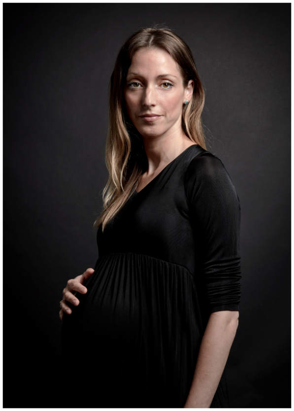 Studioporträt einer schwangeren Frau in einem schwarzen Kleid vor schwarzem Hintergrund